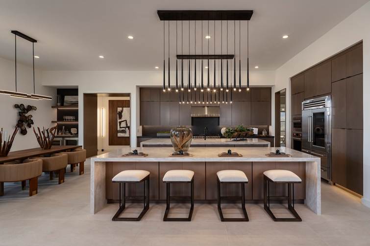 A clean and modern open-plan Denton kitchen with white marble countertops, sleek brown cabinetry, and elegant bar stools, featuring a striking linear black multi-light chandelier.