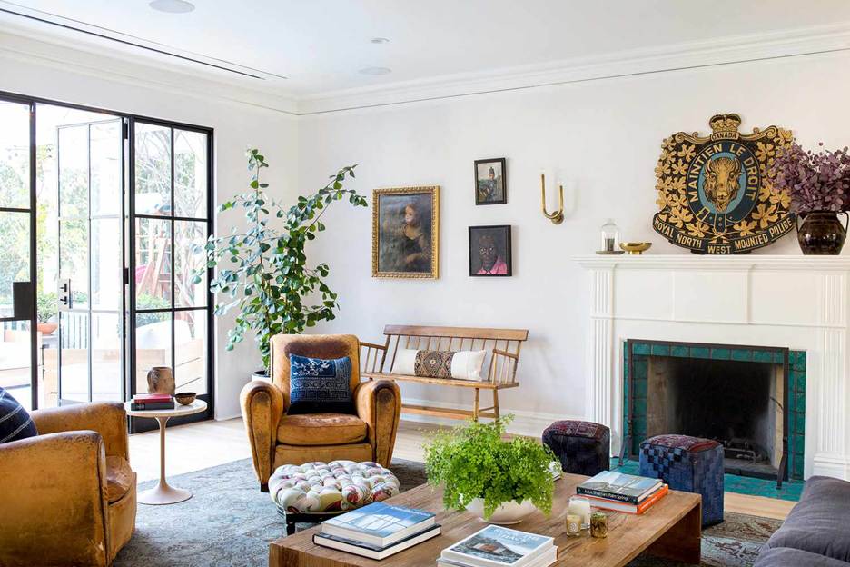 Host without the stress: A brightly lit, eclectically styled living room featuring vintage leather armchairs, a white fireplace with teal tiling, and unique wall art including a large Royal North West Mounted Police crest.