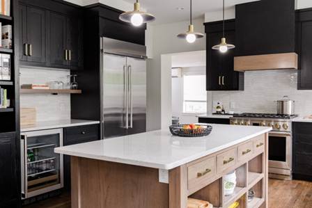 Host without the stress: A modern kitchen with dramatic black cabinetry, a natural wood island with a white countertop, and high-end stainless steel appliances illuminated by three brass pendant lights.