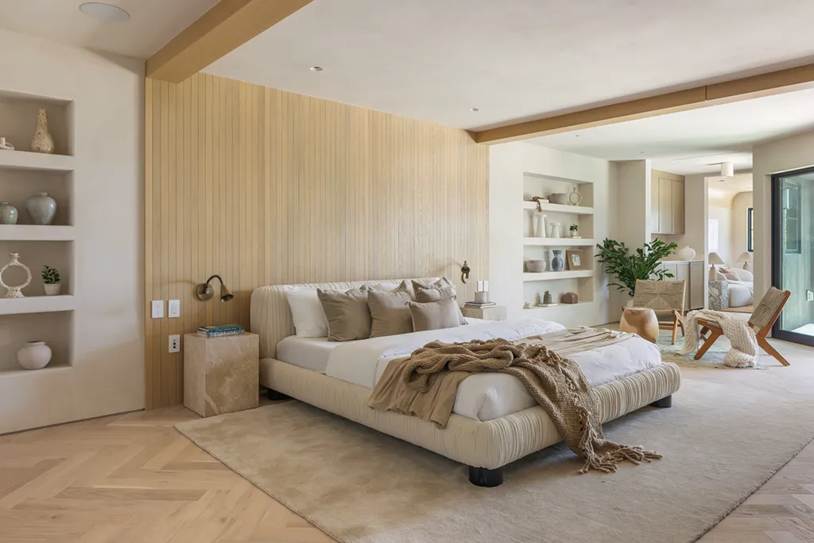 A bright, modern bohemian bedroom featuring a low-profile upholstered bed, light wood vertical paneling, built-in shelving, and neutral earth tones.