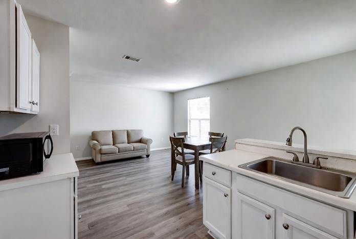 Open-concept living space with a kitchen island, dining table set, and beige sofa over wood-look flooring.
