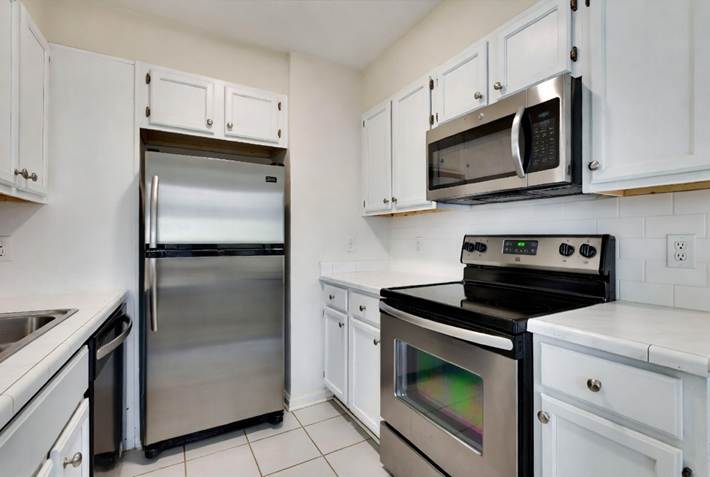 A bright kitchen with white cabinets, tile countertops, and stainless steel appliances.  August Move-In Cleanings 