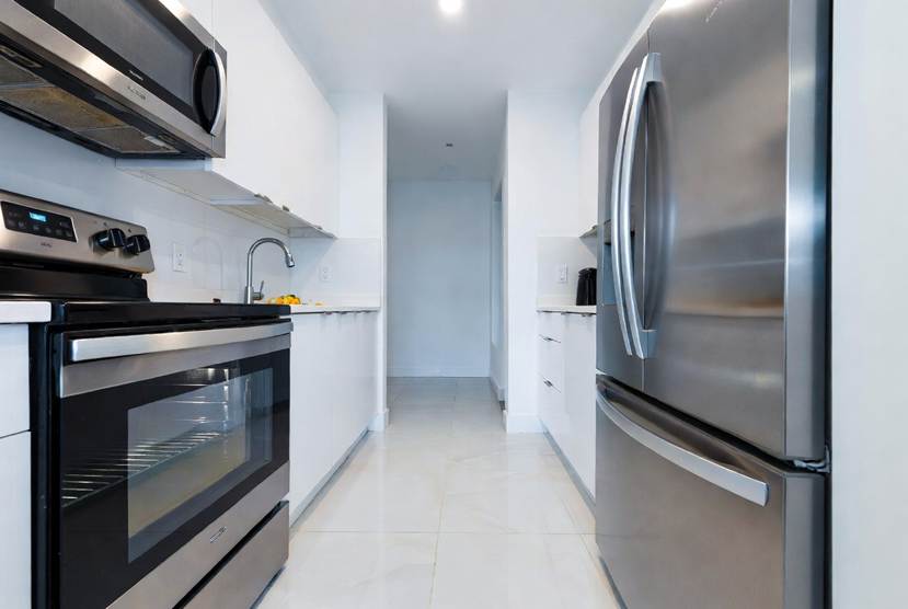 The Ultimate Denton Student Move-In & Move-Out Cleaning Checklist: Modern, clean galley kitchen featuring stainless steel appliances, white cabinetry, light tiled floors, a sleek stove with over-the-range microwave, and a double-door refrigerator.