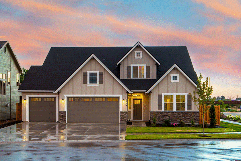 Front Porch Cleaning: Modern two-story suburban home with tan siding, stone wainscoting, and a wet concrete driveway set against a colorful sunset sky.